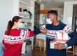 Young woman and man wearing holiday sweaters, elbow bumping and wearing masks